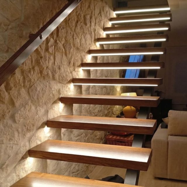 Vista detallada de una escalera de madera con luces led integradas bajo los peldaños de roble, proporcionando una iluminación ambiental cálida y moderna que resalta la textura de la madera en un espacio de diseño minimalista.