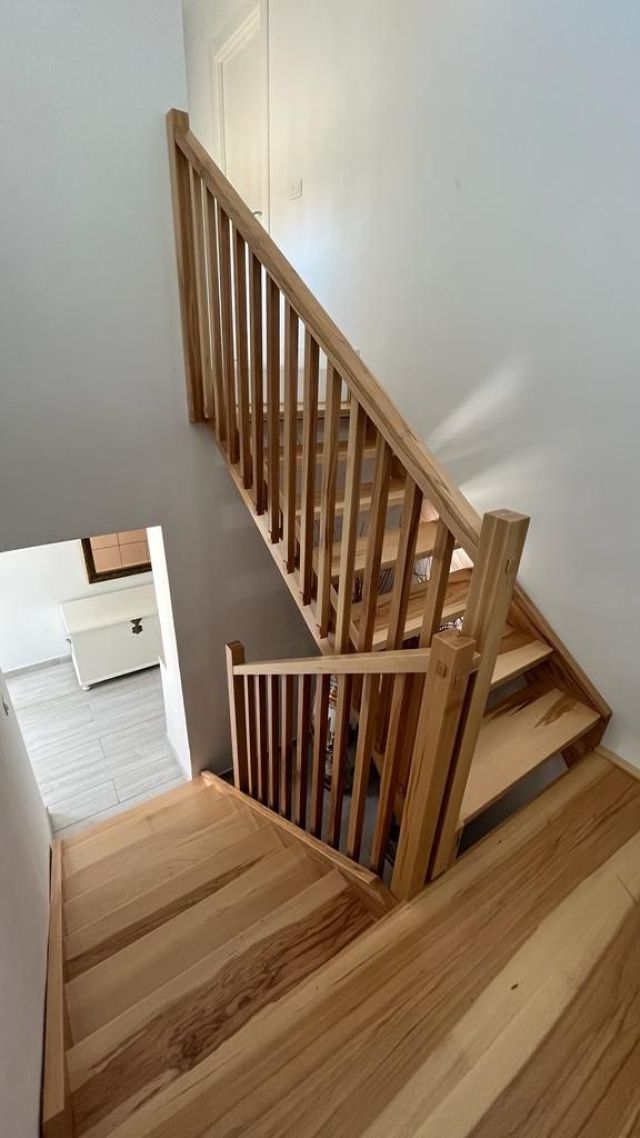 Vista de una moderna escalera de madera en haya con peldaños de tono claro y vetas marcadas y protegida por una barandilla de madera.