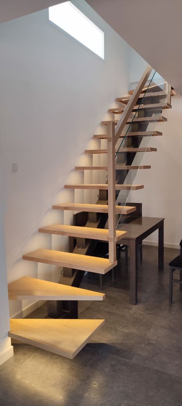 Vista de una escalera con led fabricada en madera de tono claro con peldaños flotantes, donde cada escalón cuenta con iluminación LED cálida integrada en la parte inferior, complementada por una barandilla de cristal en un ambiente de diseño de lujo.