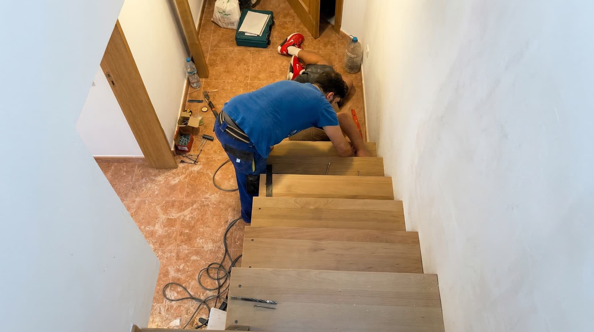Un carpintero profesional realizando la instalación de escaleras de madera en Murcia, ajustando peldaños flotantes de gran grosor en una pared interior blanca durante la fase de montaje de una obra residencial.