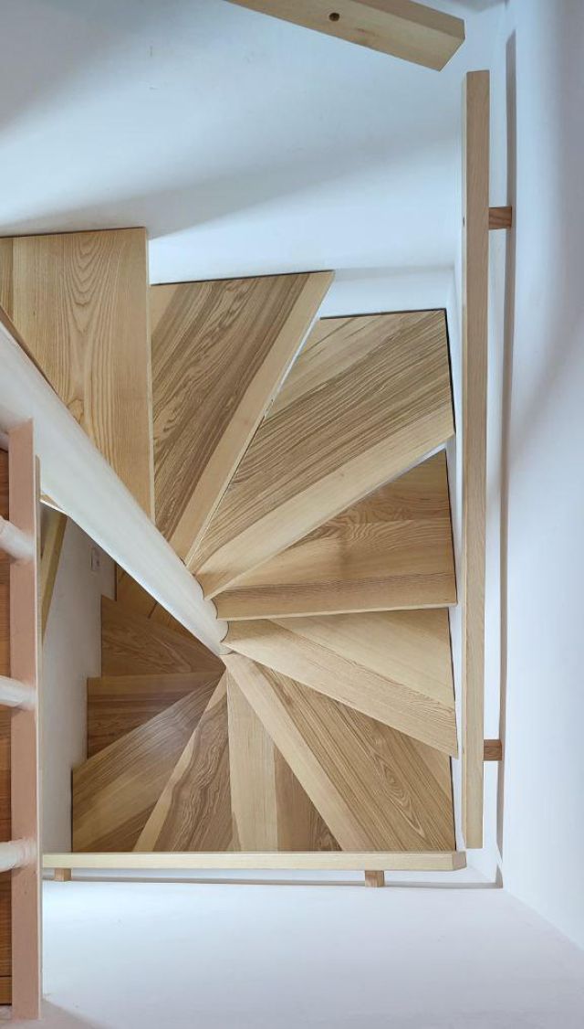 Elegante escalera de caracol moderna en madera de roble con peldaños de tono claro y veta natural, soportada por una estructura central blanca. 