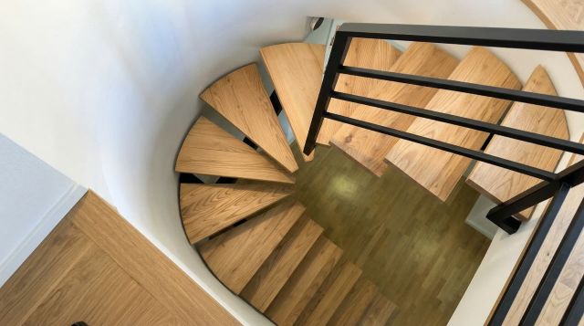 Vista de una escalera de madera en roble con forma de u de diseño moderno y artesanal, mostrando la continuidad de los peldaños y la barandilla.
